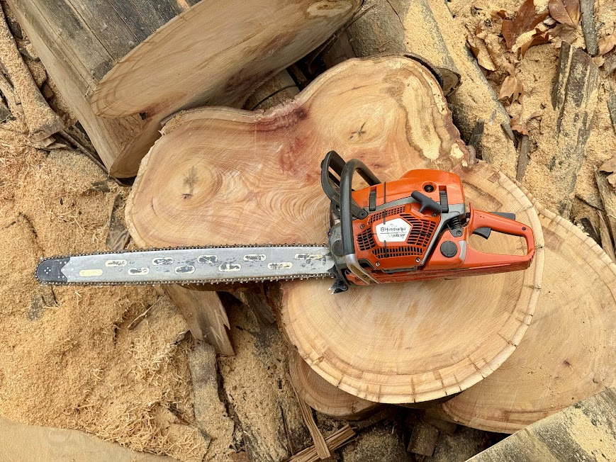 Tronçonneuse orange posée sur des rondins de bois fraîchement coupés
